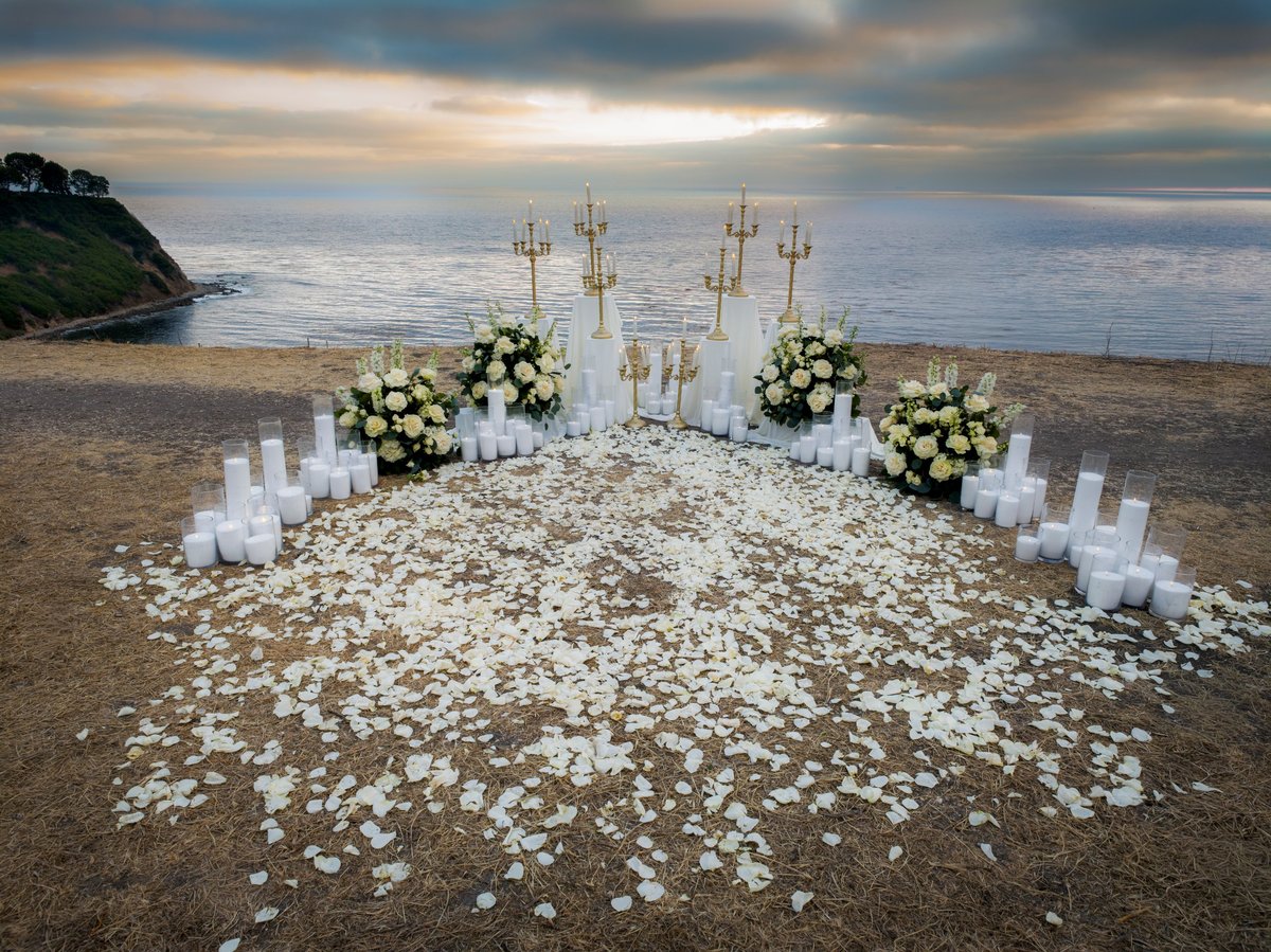 Altar de ceremonia decorado con velas y flores blancas frente al mar al atardecer